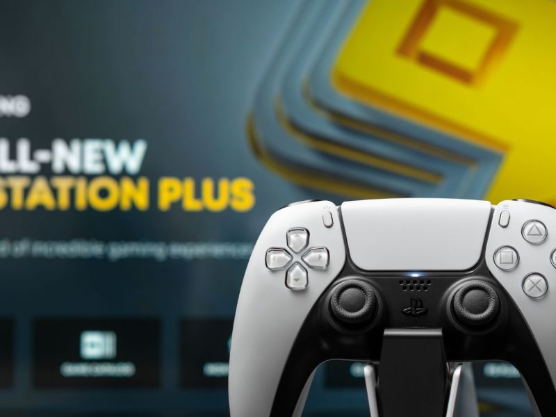 PS5-Controller, im Hintergrund Werbetafel für PS Plus.