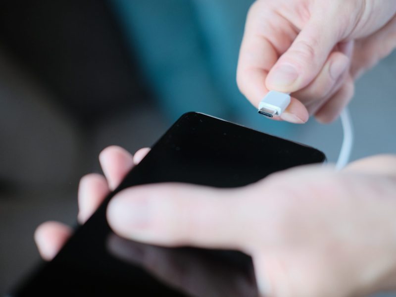 Person schlieÃŸt Ladekabel an ein Smartphone an.