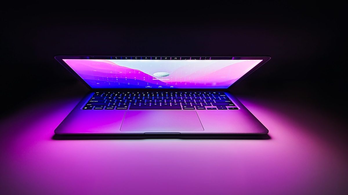 Ein halb geöffneter Apple Mac mit lila Licht vor schwarzen Hintergrund.