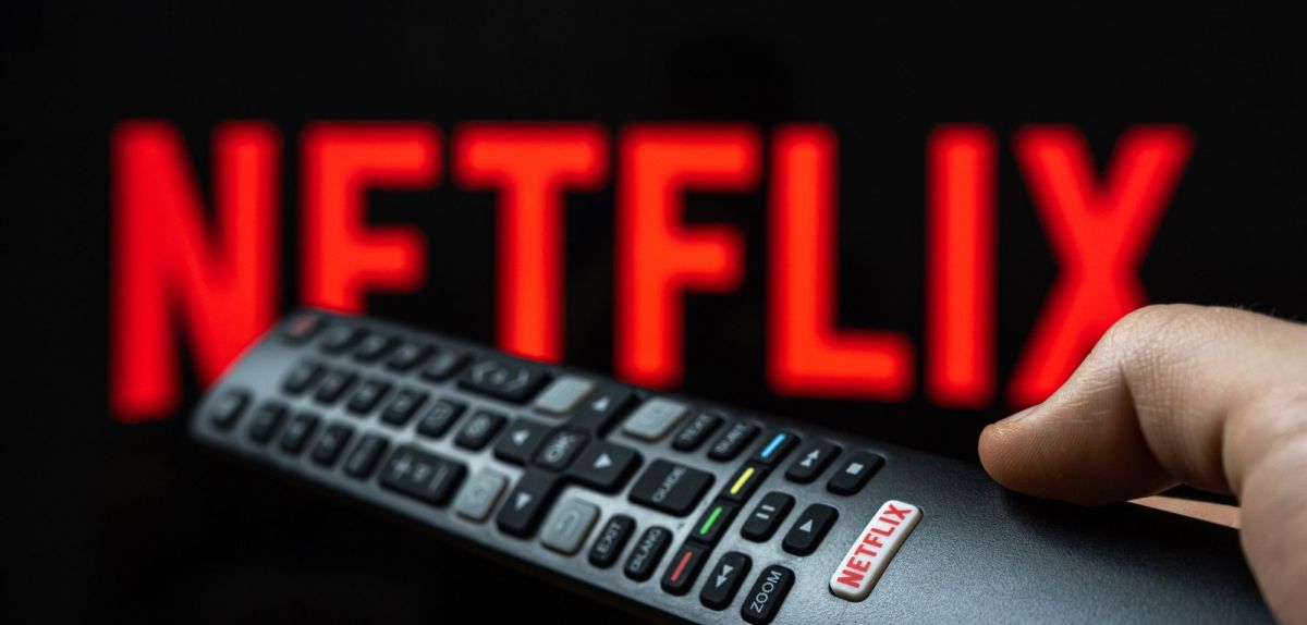 Netflix-Logo auf einem Fernseher, im Vordergrund Hand mit einer Fernbedienung.