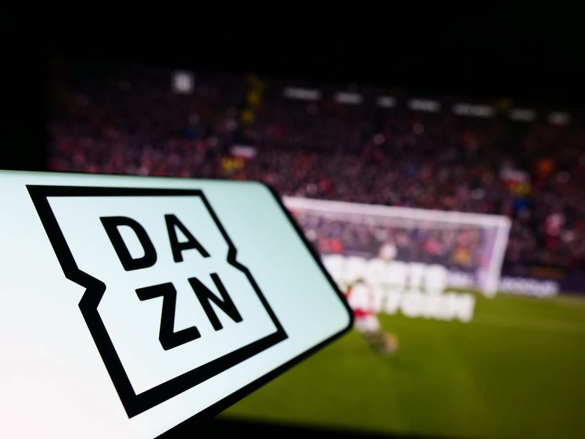 Die App von DAZN auf einem Smartphone; im Hintergrund steht ein FuÃŸballtor.