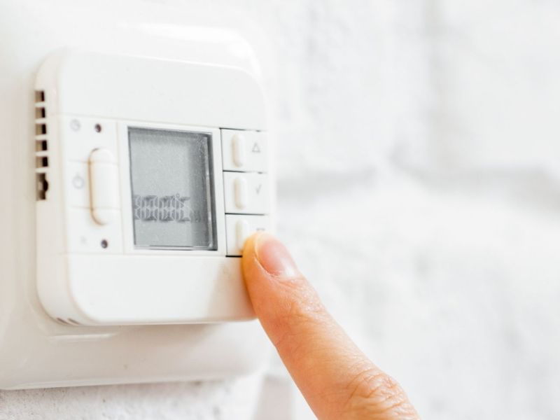 Person tippt mit dem Finger auf ein Thermostat.