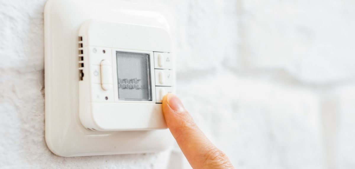 Person tippt mit dem Finger auf ein Thermostat.