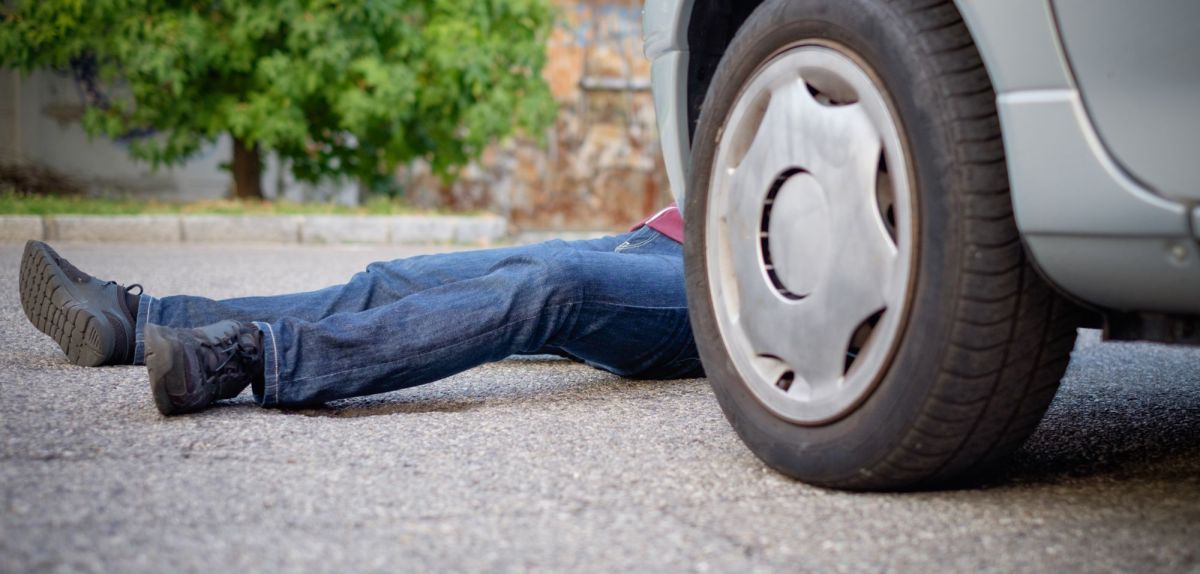 Person liegt tot vor oder hinter einem Auto.