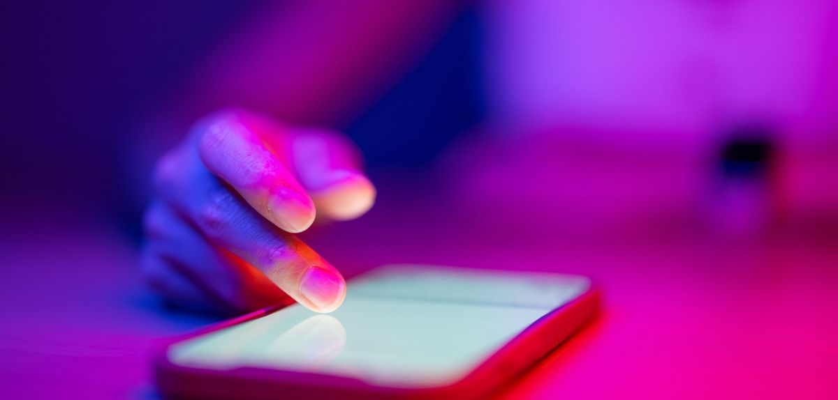 Person tippt auf ein auf einem Tisch liegenden Handy im Neonlicht.
