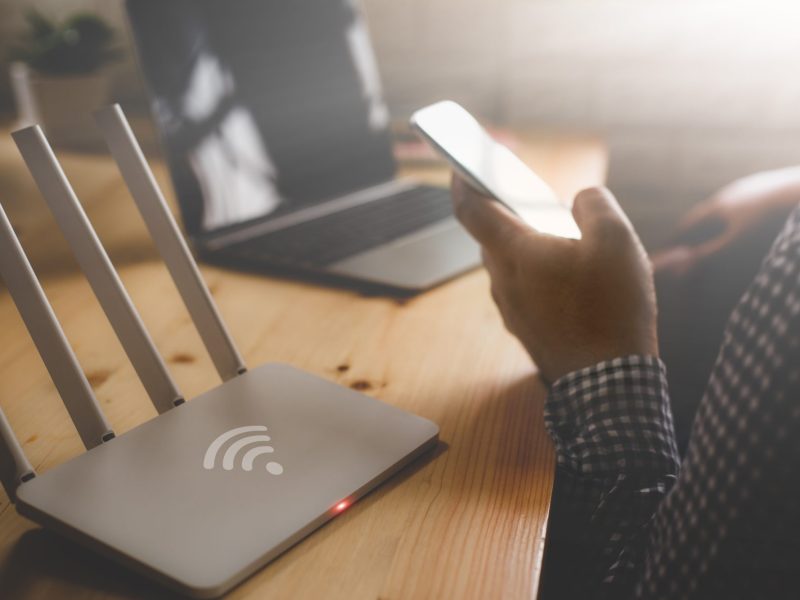 Person sitzt mit Handy vor dem WLAN-Router