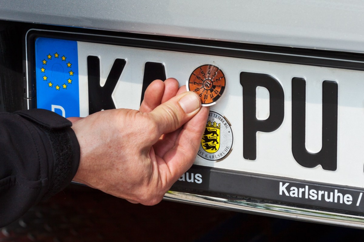 Mann klebt die HU-Plakette auf das Nummernschild