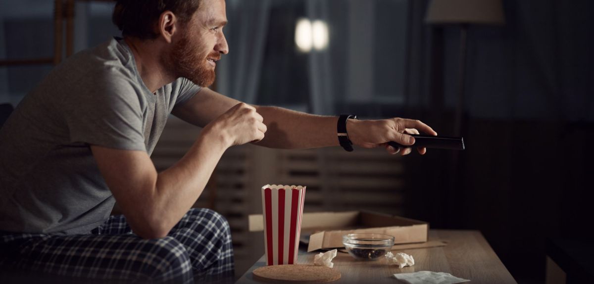 Mann sitzt abends mit Snacks vor dem Fernseher.