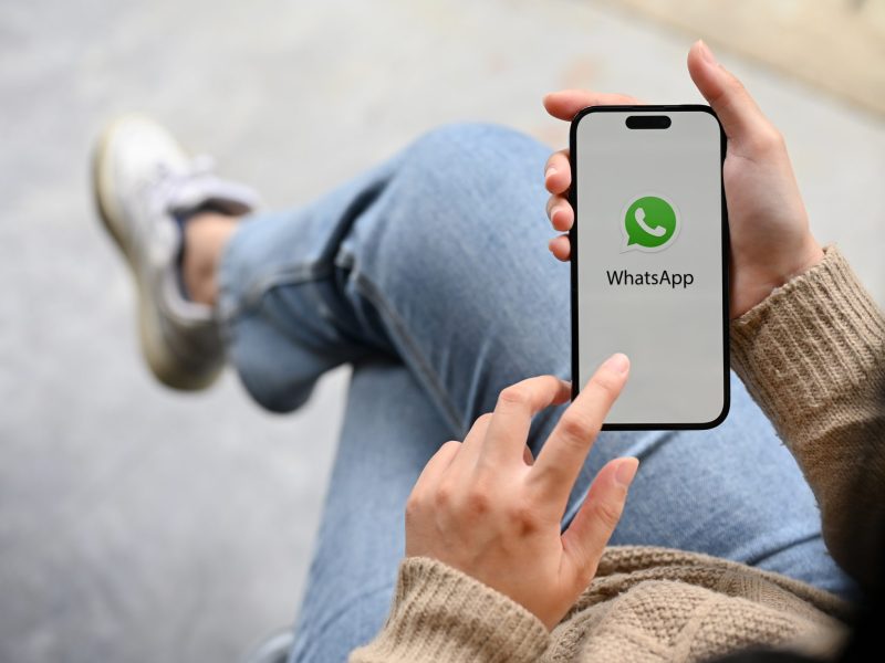 Frau hält ein Smartphone, auf dem WhatsApp geöffnet ist.