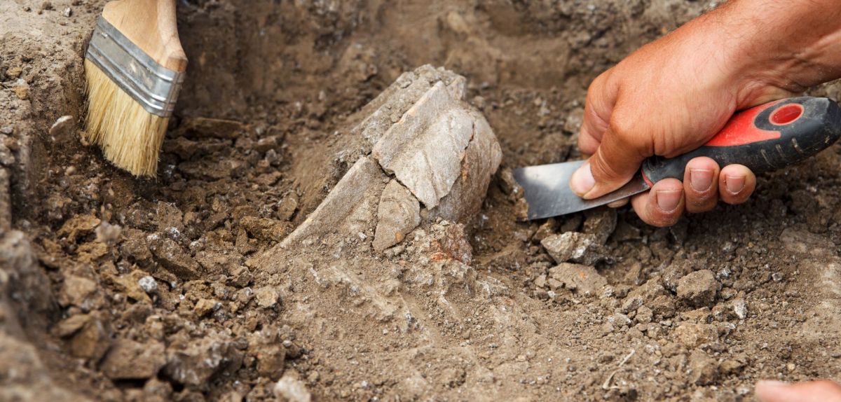 HÃ¤nde mit Werkzeugen graben an einem archÃ¤ologischen Fund.