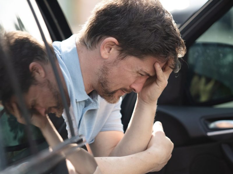 Mann sitzt aufgelöst auf dem Beifahrersitz eines Autos