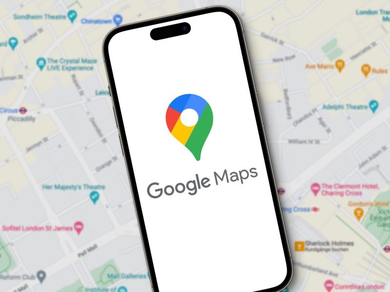 Auf einem Handy-Display wird das Google Maps-Logo angezeigt. Dahinter ist eine Karte zu sehen.