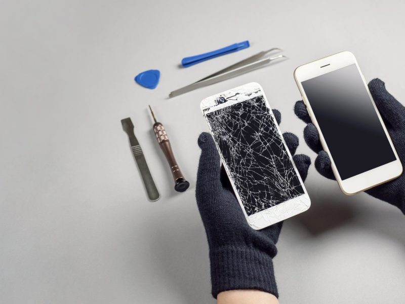 Zwei Hände halten ein kaputtes und ein heiles iPhone in der Hand. Darüber Reparatur-Werkzeug