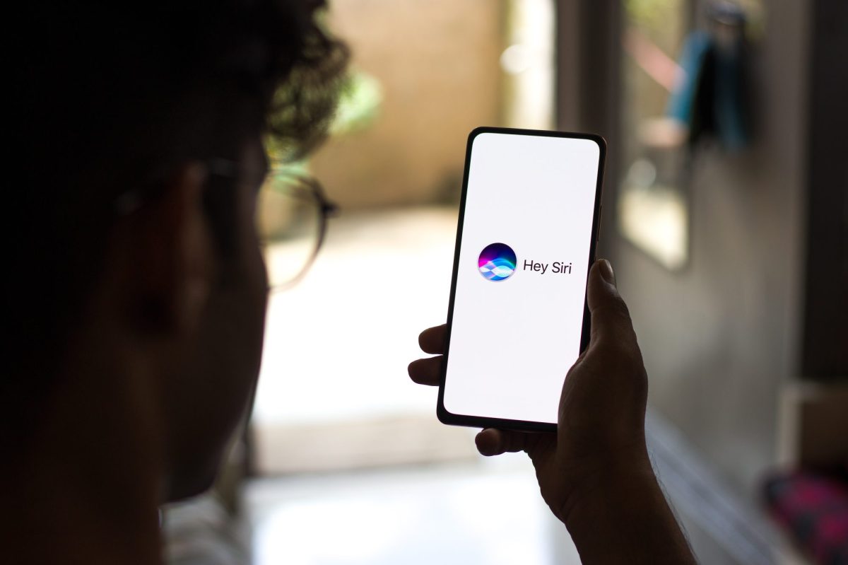 Eine Person hält ein Handy in der Hand, auf dessen Display Hey Siri angezeigt wird.