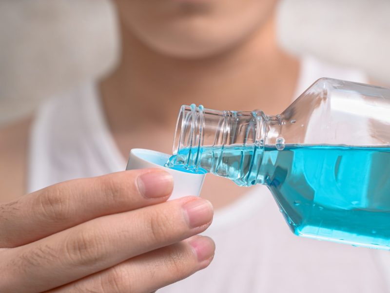 Eine Person gibt Mundwasser aus einer Flasche in eine Kappe.