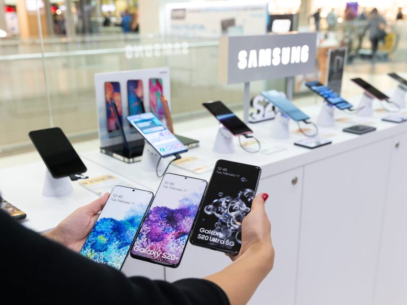 Person hÃ¤lt mehrere Samsung-Handys vor einer Auslage.