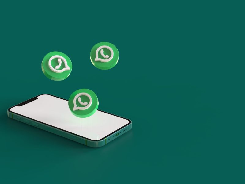 Ein Handy liegt auf einem grÃ¼nen Untergrund. DarÃ¼ber schweben drei WhatsApp-Logos.