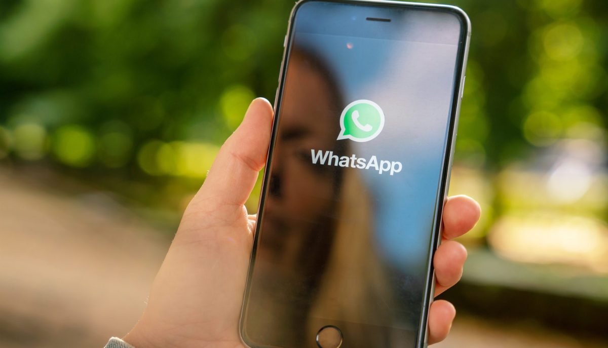 Eine Person hÃ¤lt ein Handy. Auf dessen Display wird das WhatsApp-Logo angezeigt.