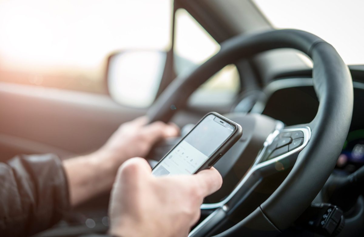 Person hält ein Handy am Steuer in der Hand.