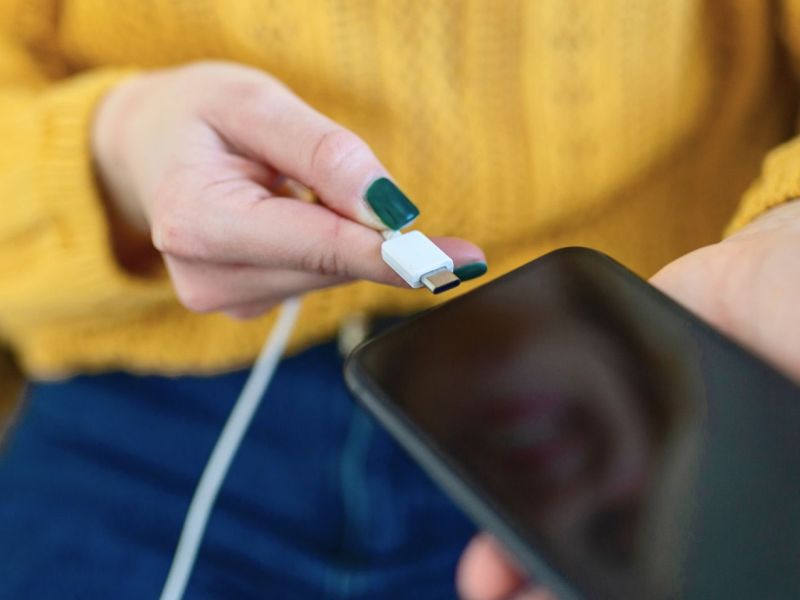 Frau steckt Handy ans Ladekabel