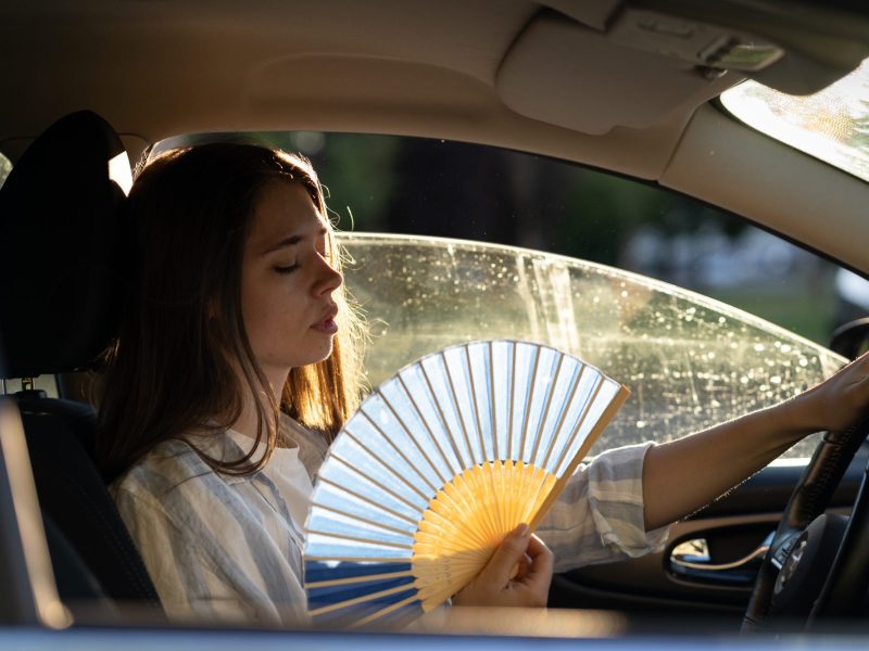 Person sitzt im Auto mit einem FÃ¤cher in der Hand.