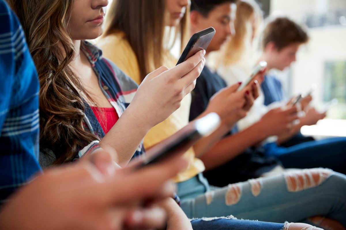 Jugendliche sitzen in einer Reihe nebeneinander und halten jeweils ein Smartphone in der Hand.