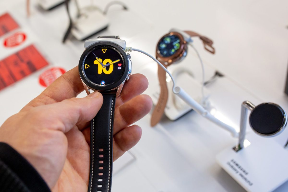 Eine Person hält eine Samsung Galaxy Watch in der Hand. Im Hintergrund sind in einer Auslage weitere Samsung Galaxy Watch-Modelle zu sehen.