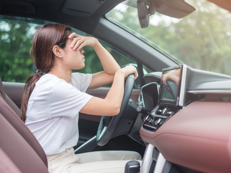 Frau sitzt am Steuer eines Autos und hÃ¤lt sich verzweifelt die Hand vor das Gesicht.