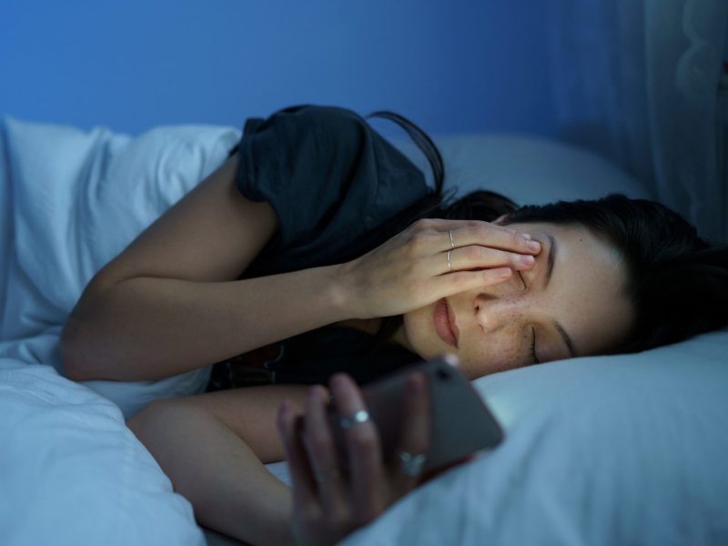 Person liegt im Bett und hÃ¤lt ein Handy in der Hand.