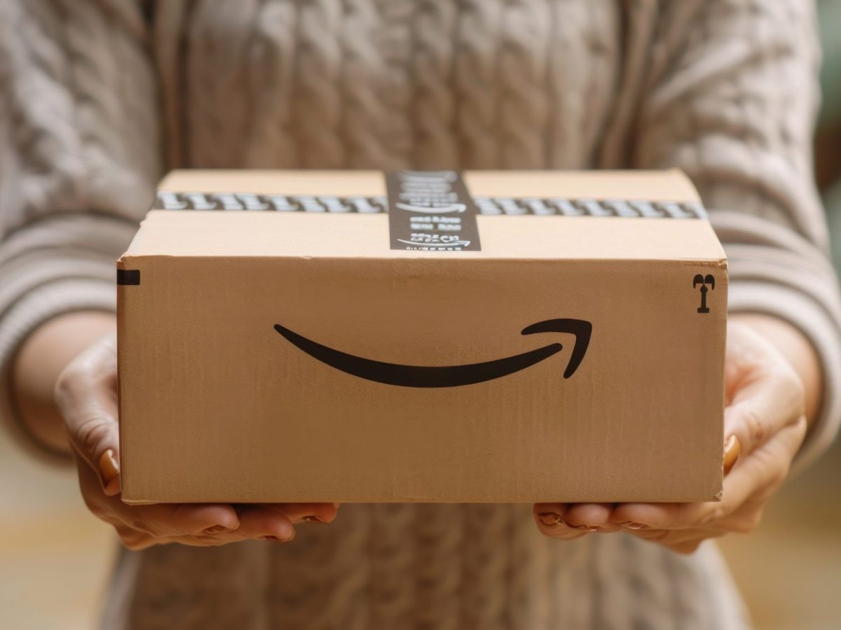 Eine Person hält einen Karton, auf dem das Amazon-Logo abgebildet ist.