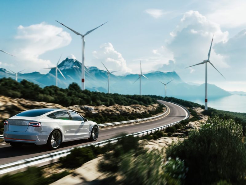 Elektroauto auf einer Autobahn mit WindrÃ¤dern im Hintergrund.