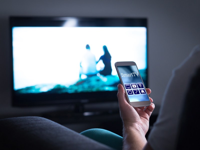 Person hÃ¤lt ein Smartphone vor einen Fernseher