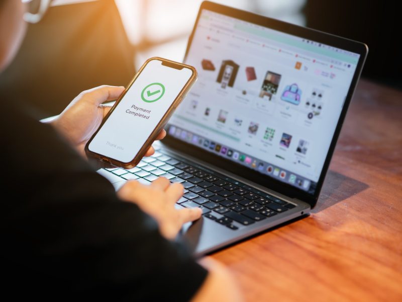 Person sitzt vorm Laptop und bezahlt Online via Handy.