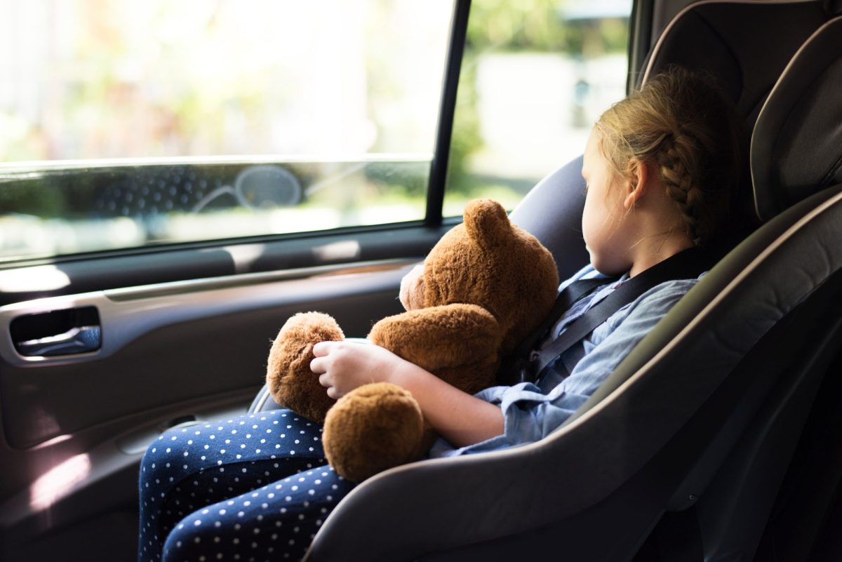 MÃ¤dchen sitzt in einem Auto-Kindersitz und hÃ¤lt einen Teddy in der Hand, wÃ¤hrend sie aus dem Fenster guckt.