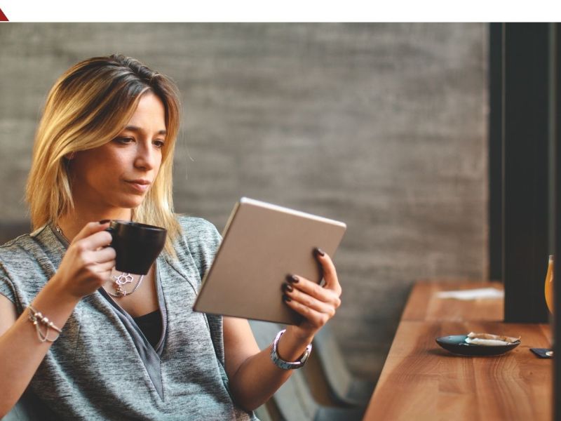 Frau sitzt entspannt am Tisch mit einem Tablet in der Hand.