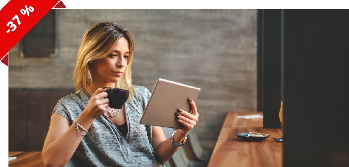 Frau sitzt entspannt am Tisch mit einem Tablet in der Hand.