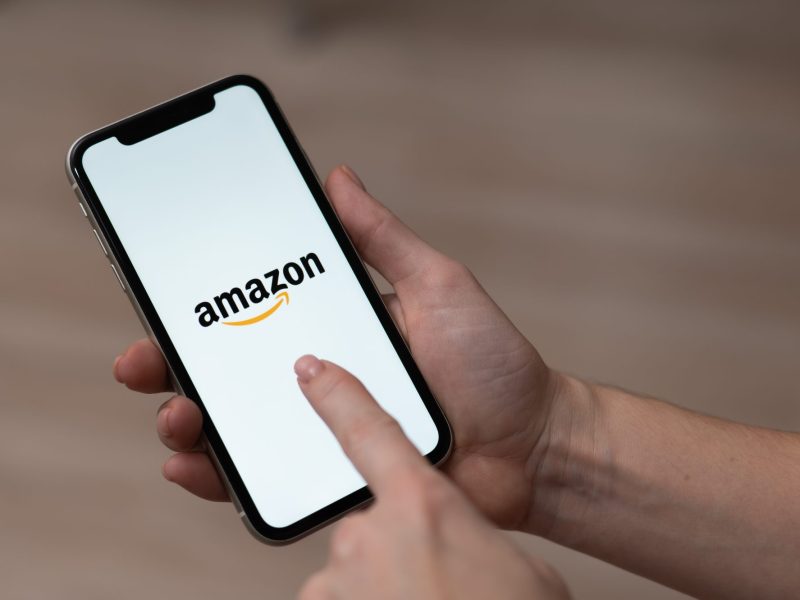 Person hält ein Handy in der Hand. Auf dem Display wird das Amazon-Logo angezeigt.