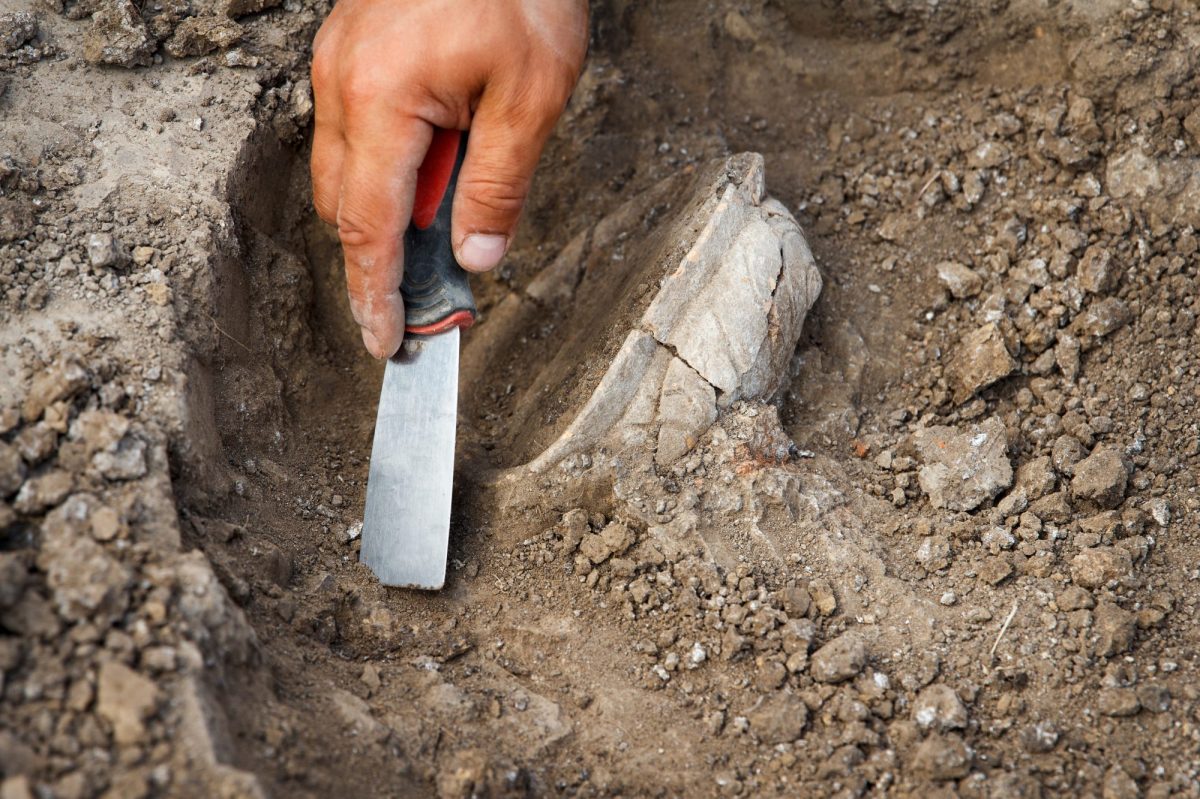 Person arbeitet mit Spaten an einem archäologischen Fund.