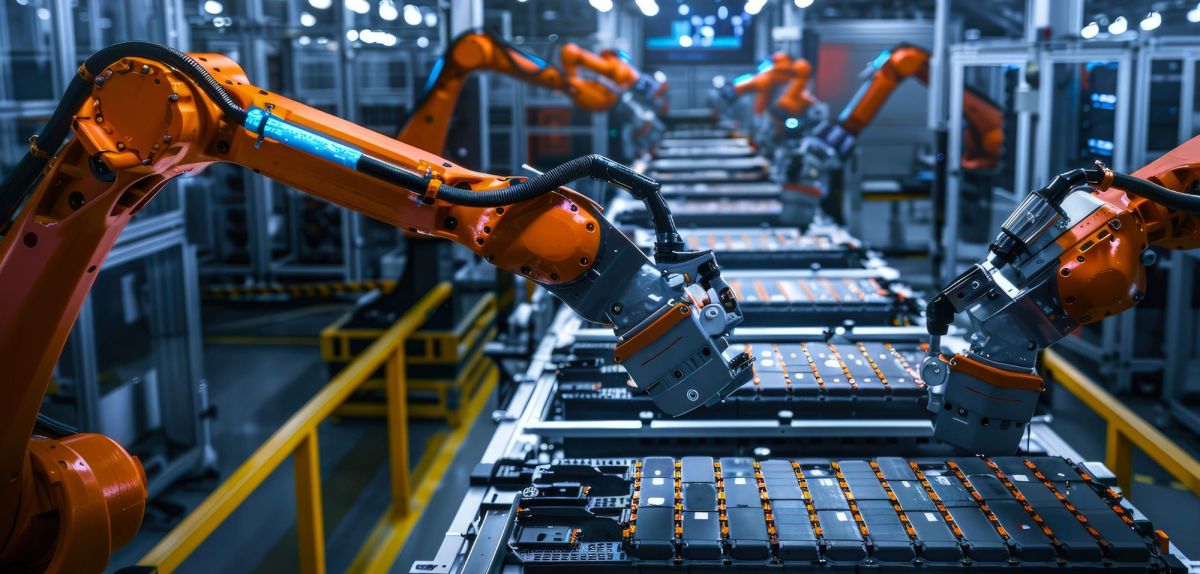 Montagelinie mit Roboterarmen, die Batteriezellen für Elektrofahrzeuge in Gehäusen handhaben und positionieren, unter heller Industriebeleuchtung