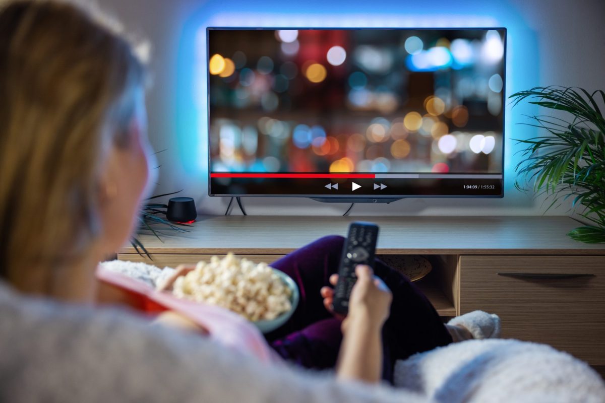 Frau guckt auf einen Fernseher mit Popkorn in der Hand.