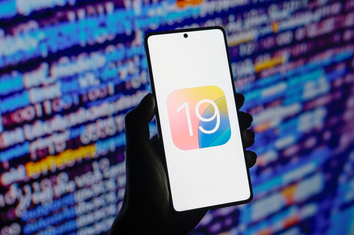 iOS 19-Logo auf einem Smartphone-Display. Im Hintergrund sind Code-Zeilen zu sehen.