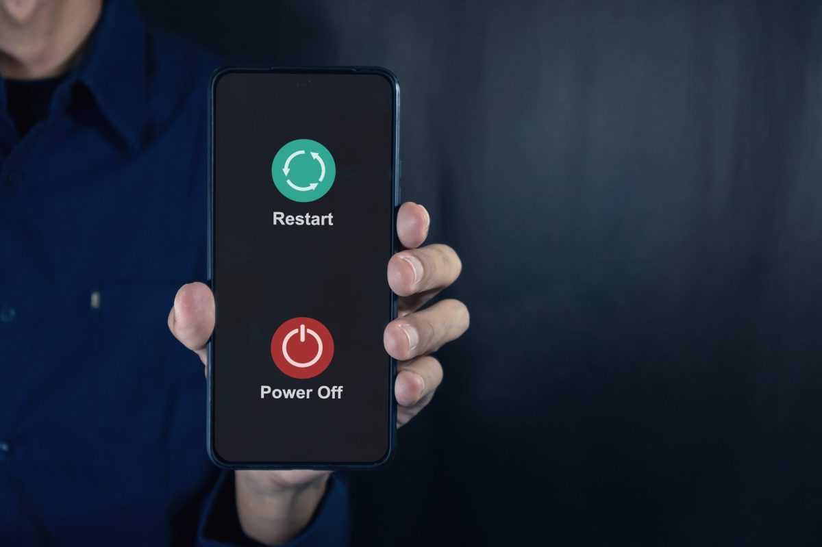Eine Person hält ein Handy in der Hand. Auf dessen Display werden die Optionen angezeigt, das Handy auszuschalten oder neu zu starten.