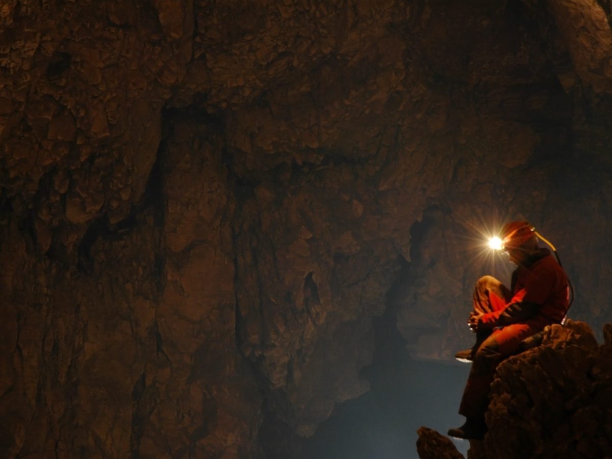 Forscher*in mit Helm und Stirnlampe sitzt in einer Höhle. (Symbolbild)