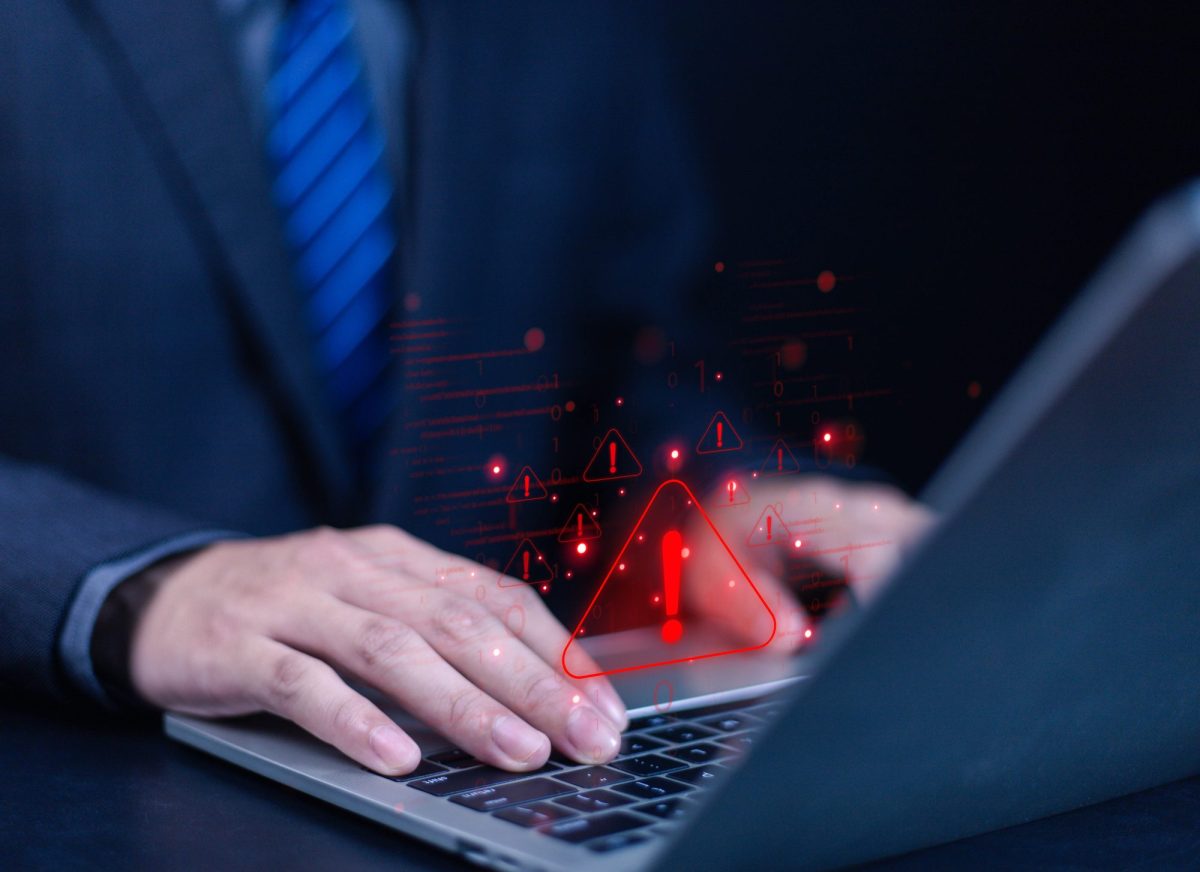 Person tippt an einem Laptop. Über dem Bild liegt ein rotes Warndreieck mit Ausrufezeichen in der Mitte.