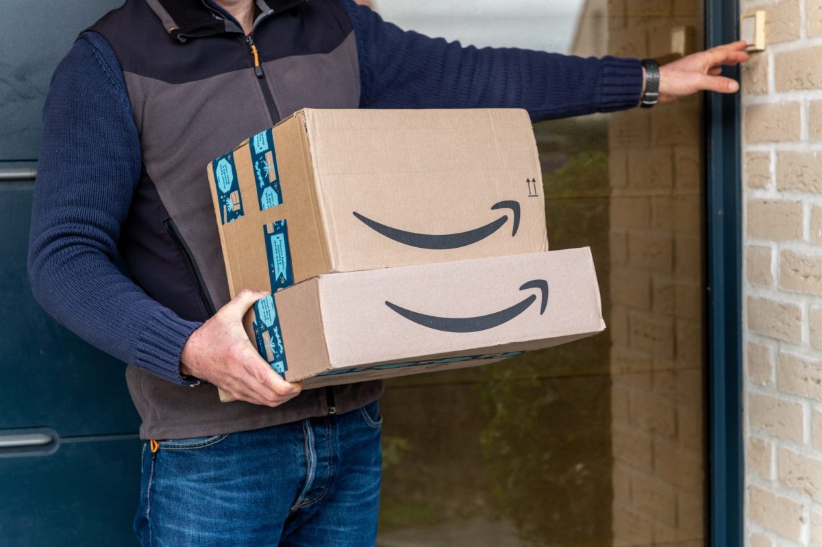Person hält Amazon-Pakete in der Hand und klingelt an einer Tür.