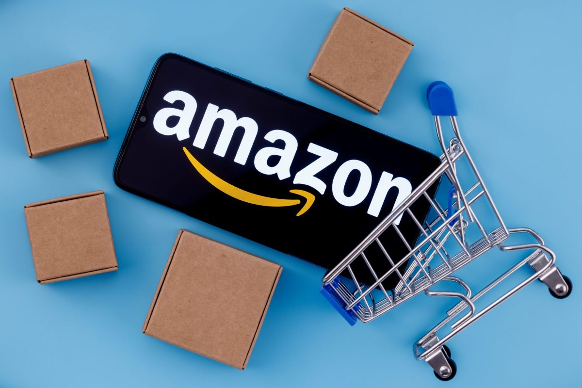 Handy mit Amazon-Logo liegt neben einem Einkaufskorb und Kartons.