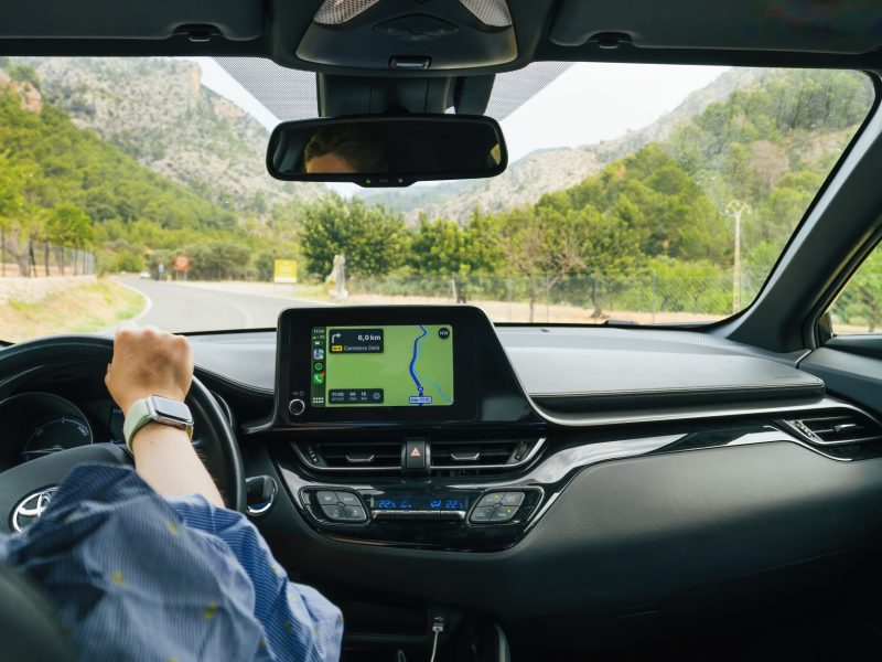 Person sitzt am Stuer eines Autos. Auf dem Fahrzeug-Display ist eine Navigations-App geöffnet.