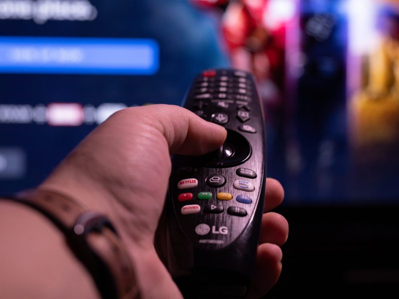 Person hält eine LG-Fernbedienung in der Hand und richtet sie auf einen Fernseher.