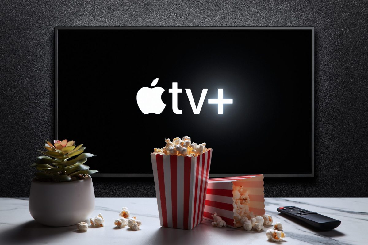 Apple TV+ wird auf einem Fernseher angezeigt. Auf einem Tisch davor steht Popcorn.
