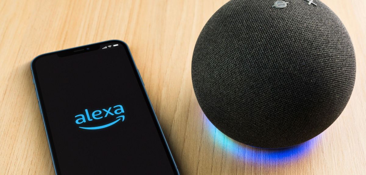 Amazon Alexa wird auf einem Handy-Display angezeigt. Daneben steht ein Amazon Echo-Gerät.